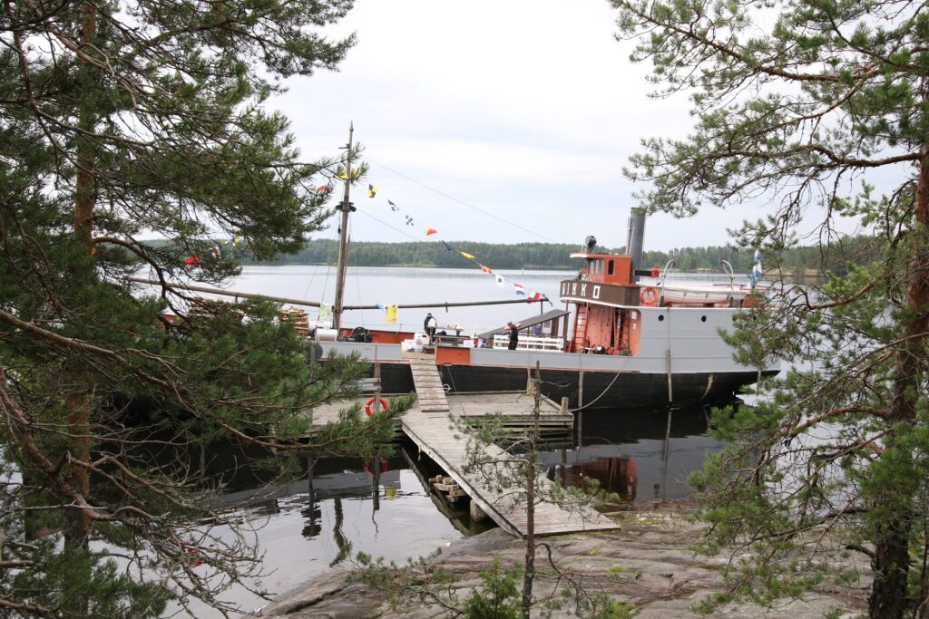 Vanha höyrylaiva laiturissa kaunissa järvimaisemassa.