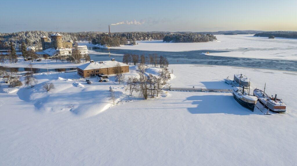 Vanhoja rakennuksia ja laivoja talvisessa maisemassa järvellä.