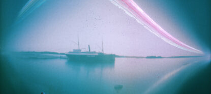 Utuinen värikuva, jonka keskellä vanha höyrylaiva laituriin kiinnittyneenä. Laivan yli kulkee sateenkaarimainen paksu juova, joka nousee keskellä laivan yläpuolella kaareksi.