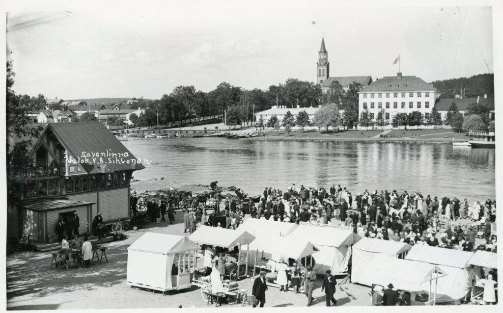 Paljon ihmisiä sekä torikojuja. Taustalla vettä sekä kirkontorni.