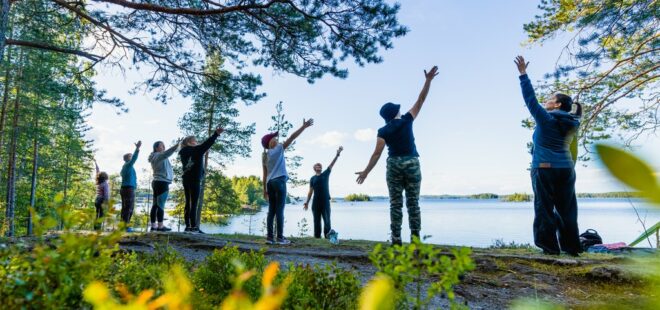 Ihmiset venyttelevät luonnossa kallion päällä seisoen.
