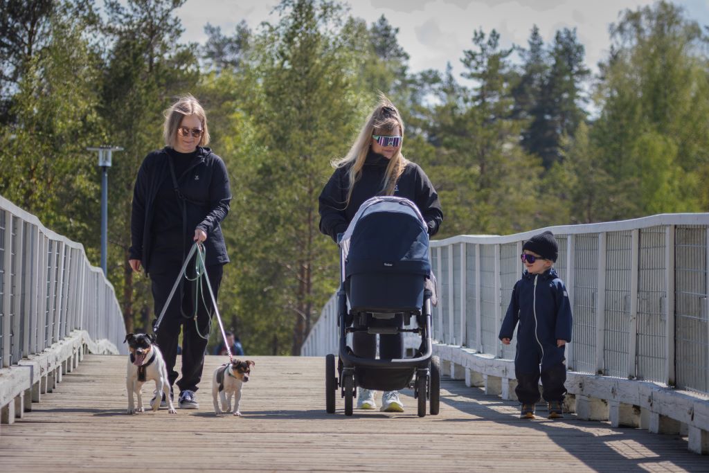 Kaksi naista ja lapsi kävelemässä puusillalla.